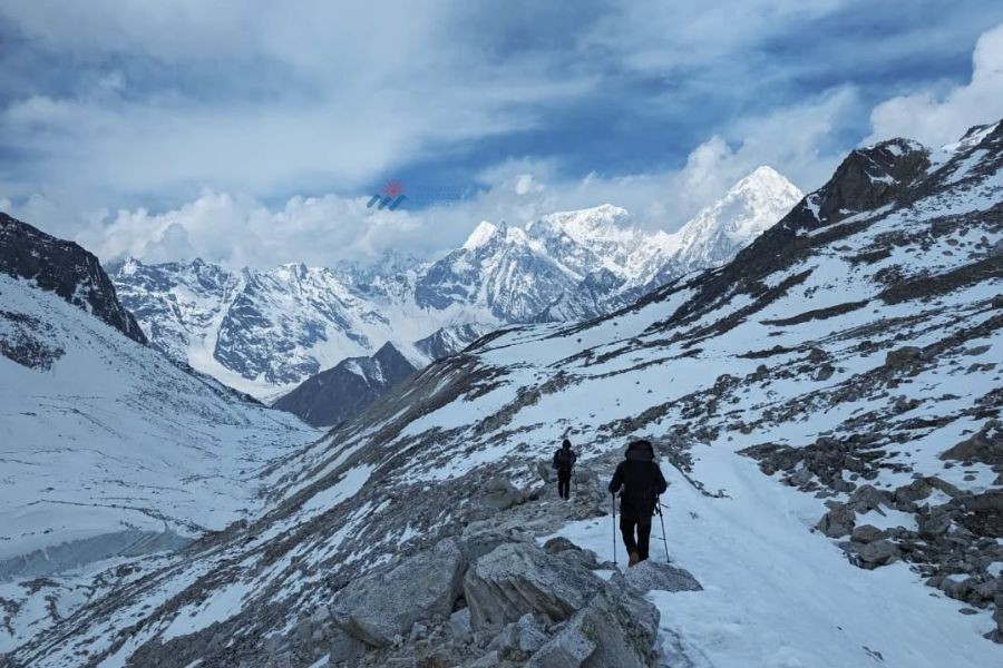 Two trekkers walking on a snowy mountain trail with Himalayan peaks ahead